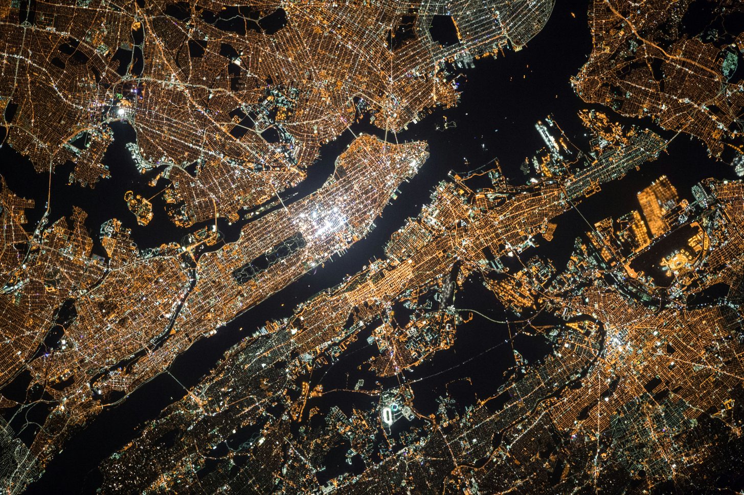 Aerial night view of a dense grid of amber and white lights spread across dark water
